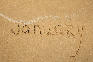 January - handwritten on the soft beach sand.