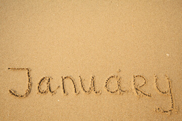 January - handwritten on the soft beach sand.