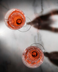 Rose wine in fancy crystal flutes on rich Carrera marble background with creative shadow effect.