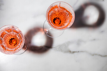 Rose wine in fancy crystal flutes on rich Carrera marble background with creative shadow effect.
