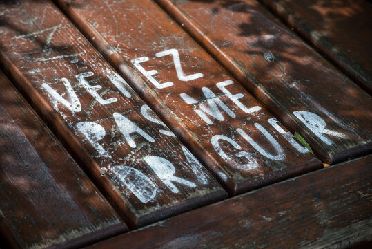 Closeup of french inscription on a wooden bench : venez pas me draguer, in english : don't come flirt with me