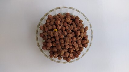 Bunch of organic fresh boiled and dried black or brown chickpeas, chana, Bengal gram seeds isolated on glass bowl placed on white abstract table background. Horizontal closeup macro flat lay top view.