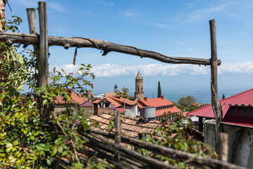 Roofs of houses and domes of ancient churches in Georgia framed by a wicker fence made of tree