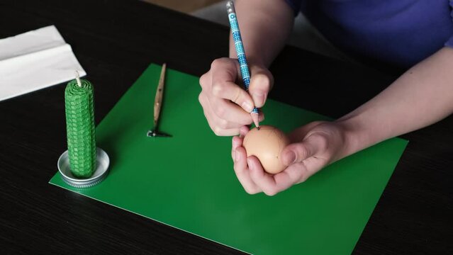 The girl uses a pencil to mark the pattern on the egg to create an Easter egg.