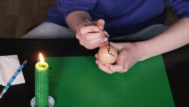 Melting the wax over the candle, with the help of a pen, the girl puts a pattern on the Easter egg.