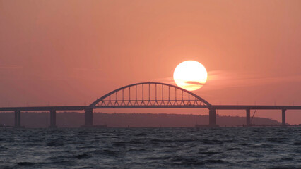 Stunning view of the beautiful sunset over the big river and the bridge, time lapse effect. Shot. Bright golden sun moving towards the horizon above the river.
