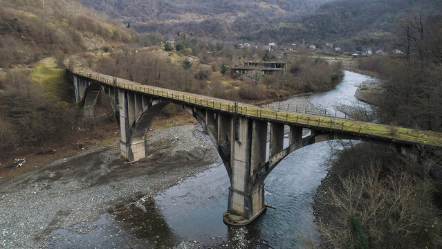 Aerial view of the village and mountains covered by yellow trees and a narrow river flowing under the old mossy bridge. Shot. Ecology and drying up of the reservoirs concept,