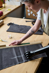 Female fashion designer bending over table with textile workpiece and ruler while working over new fashion collection or order of client