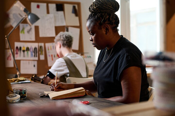 Serious African American female tailor or designer looking through lookbook while thinking of new...