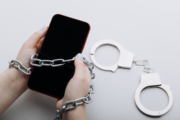 Smartphone with chain locked and handcuffs in woman's hand. Information security or smartphone...