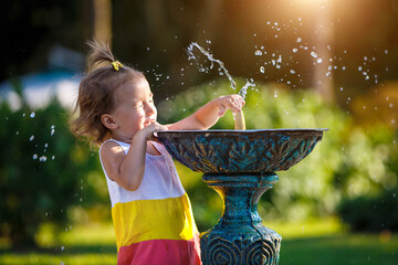 A funny little girl is playing with the spray of a drinking water fountain in the park. Childhood,...