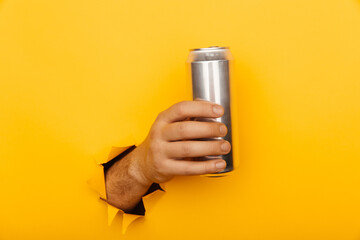 Hand holds metal jar in torn hole of yellow background