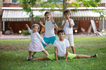 Three young boys and toddler girl making funny faces outdoors. Friends or siblings having fun.