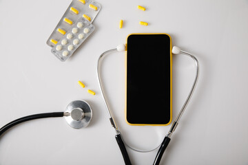 Online doctor consultation concept. Stethoscope and smartphone with pills on a white table. Top view
