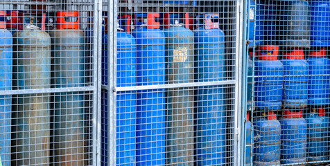 Group of blue colored propane gas cylinders with red handle behind metal bolt and bar