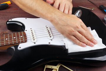 Guitar master wipes surface of black electric guitar with rag.