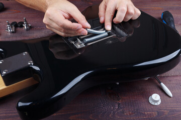 Guitar technician adjusts springs of tremolo bridge on electric guitar.