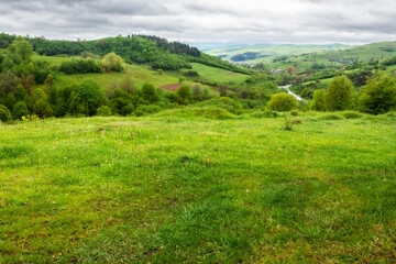 Fototapeta na wymiar countryside landscape on a cloudy day in mountains. village in the distant valley. green nature scenery in spring. grassy meadows and trees on the hills