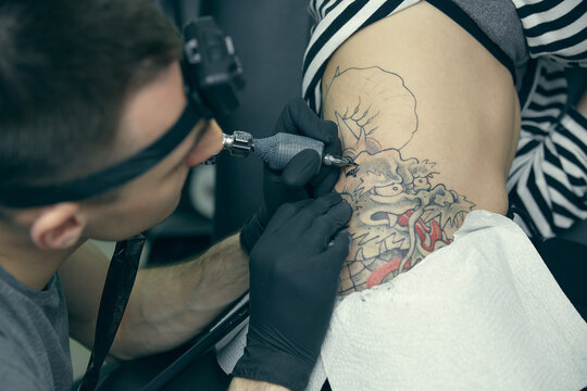 The master creates a picture on the body of a young beautiful girl. Close-up of hands and tattoo machine