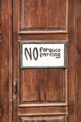 No parking sign on a  brown wooden doorframe in both english and spanish language, stylish and relaxed sign