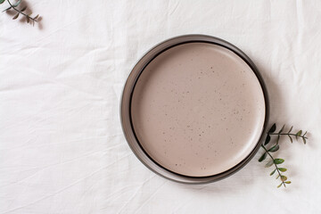 Empty ceramic plate and eucalyptus branches on a white cloth. Top view