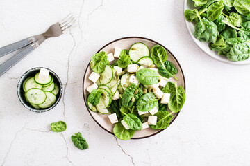 Fresh salad of cucumbers, spinach, cheese and pumpkin seeds in a plate. Top view