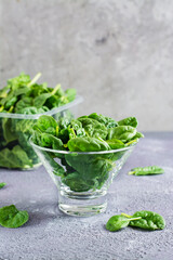 Fresh baby spinach leaves in a glass bowl and behind on a texture table. Vertical view