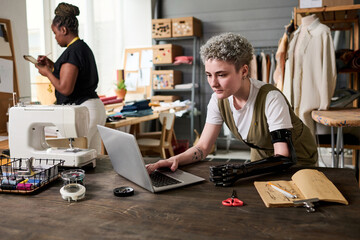 Young female fashion designer with myoelectric arm looking for new ideas in the internet while...