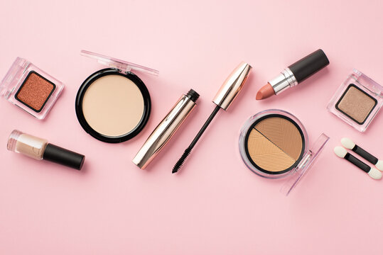 Make up concept. Top view photo of lipstick compact powder blush eyeshadow brushes nail polish and mascara on pastel pink background