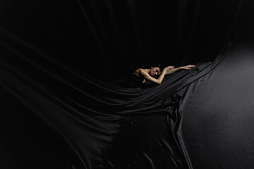  ballerina lies on a black satin fabric