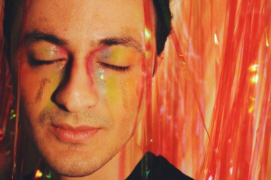 closeup portrait of young queer nonbinary person with lgbtqia+ rainbow pride flag eye makeup 