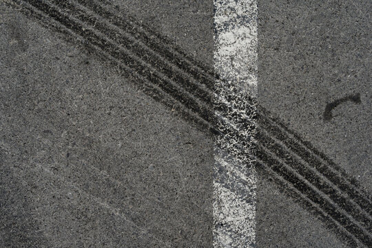 Asphalt texture with white line and tire marks. Smooth asphalt road. Tarmac dark grey grainy road background.Top view