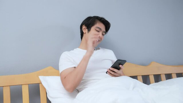 Holiday concept of 4k Resolution. Young Asian man playing mobile phone in bedroom.