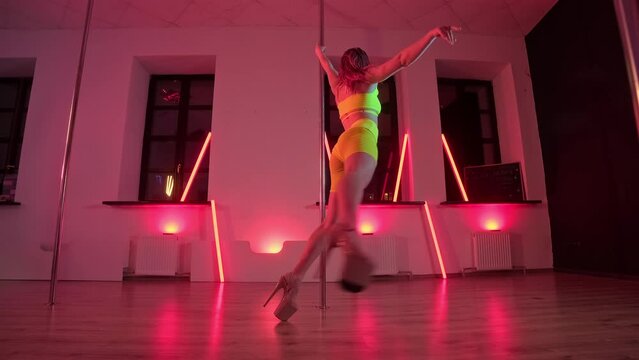 Sexy female pole dancing on red background. Elegant woman dancing near pole with red light at background. Sensual dance. Dance and acrobatics concept. 4K, UHD