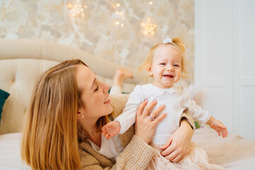 Cute mom and baby daughter lie down, play and hug in bed. games with children. 