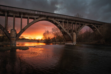 Fototapeta na wymiar Old arch bridge in a view of sunset stormy sky