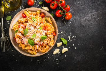 Italian pasta alla arrabiata with fresh tomatoes, basil and parmesan on black stone table. Flat lay with copy space.