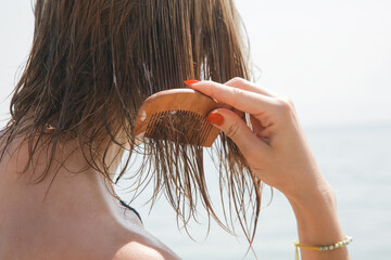 Woman's hair on the beach. Woman applaying hair mask with wooden comb. Hair damage due to salty...