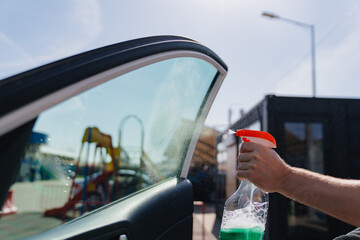 self-service car wash. a man washes the car window with glass cleaning liquid