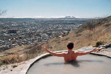 view from back. a man bathes in a hydrogen sulfide thermal spring.