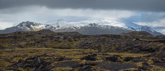 View during auto trip in West Iceland, Snaefellsnes peninsula, View Point near Svortuloft Lighthouse. Spectacular black volcanic rocks and snowy Snaefellsjokull Volcano in far.