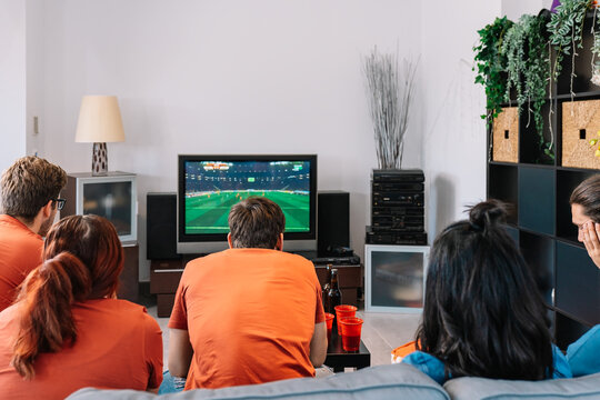 friends concentrating on watching a football match on television at home. young people. concept of leisure