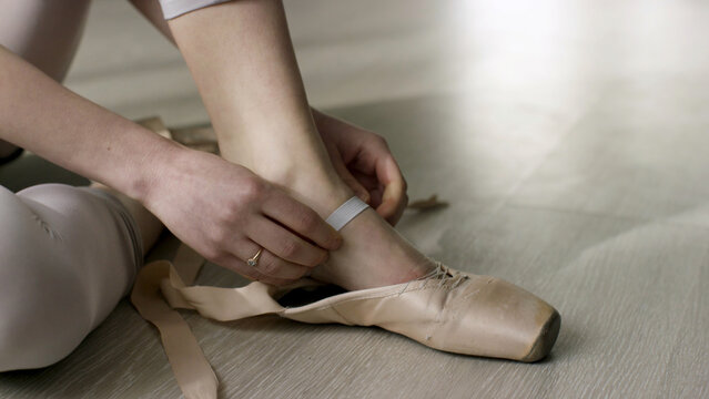 Close up for ballet dancer putting on, tying ballet shoes. Ballerina putting on her pointe shoes sitting on the floor.