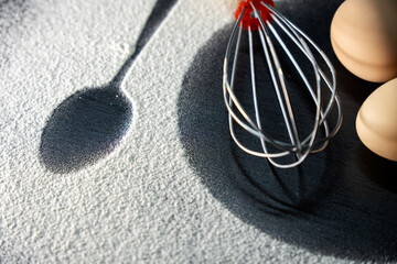 Top view of spoon and fork silhouette made with flour and egg on dark background. Egg and whisk on white flour. Rustic contrasting background. Food preparation process. Concept of bakery.