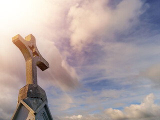 Stone cross on a top of a church, dramatic cloudy sky in the background. Catholic religion symbol.