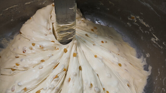 Close up for the prosess of mixing pastry with raisins in metal bowl, nutritious food concept. Stock footage. Raw dough mixing process at the factory.