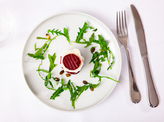 Fresh beetroot and goat cheese salad served on plate and decorated with arugula sprigs. Over white background.
