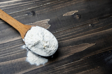 Whole flour in spoon on dark vintage wooden background. Close up view. Preparations for homemade baking. Basic ingredients for baking. 
Wheat flour on wooden spoon. 