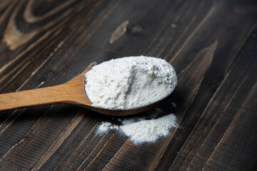 Whole flour in spoon on dark vintage wooden background. Close up view. Preparations for homemade baking. Basic ingredients for baking. 
Wheat flour on wooden spoon. 