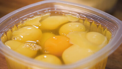 Close up for egg yolks in the plastic container, cooking concept. Stock footage. Raw fresh eggs ready for food preparation at the kitchen.